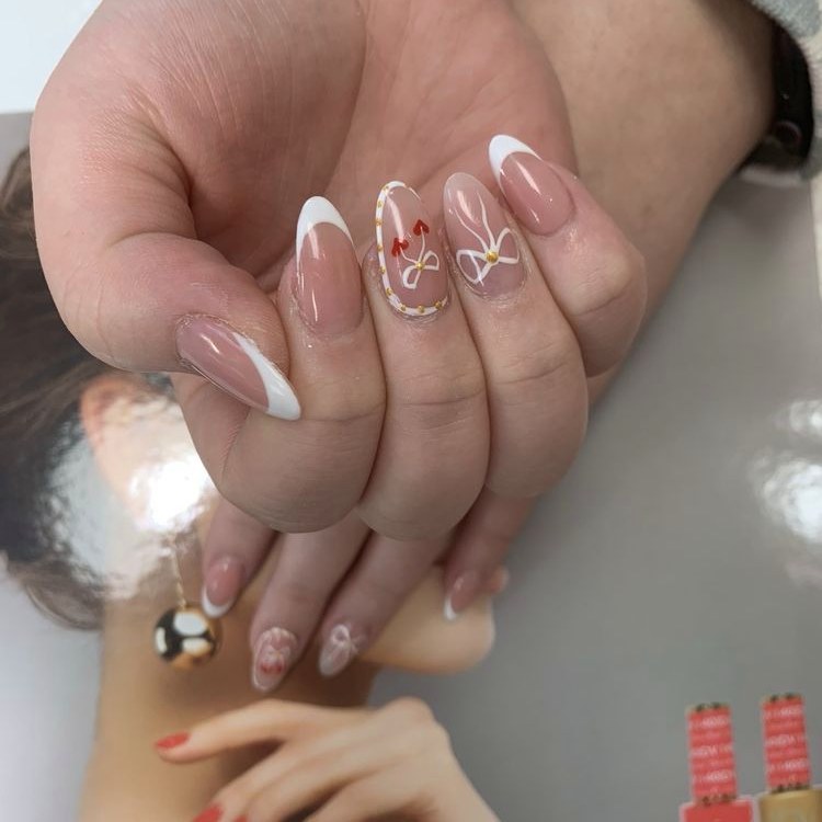 Nude almond nails with hand-painted white bows and red hearts